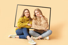 Portrait Of Young Sisters With Photo Frame On Color Background