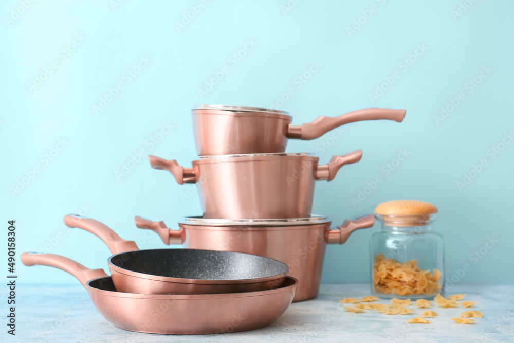 Set of copper kitchen utensils and jar with raw pasta on table against blue background