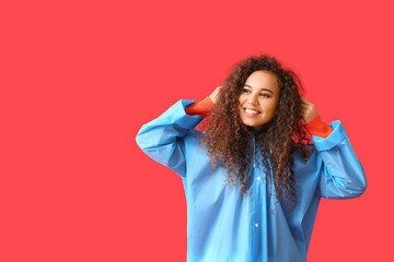 Poster - Young African-American woman in blue raincoat on red background