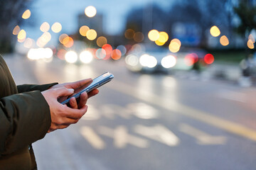 Close-up image of a woman's hands using smartphone at night on the city street, search or social networking concept, woman asking for transport via mobile application