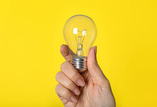 Woman Holding Incandescent Light Bulb On Yellow Background, Closeup