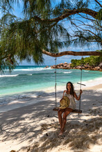 Attractive Young Woman Wearing Beach Clothes, Sitting On Swing On Paradise Beach On Tropical Island