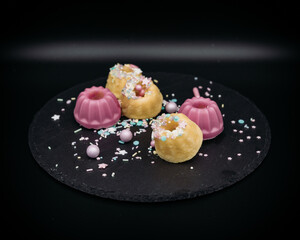 Poster - Closeup shot of pink and yellow biscuits on a black plate