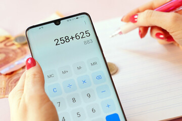 Wall Mural - Closeup shot of a woman holding a phone with a calculator on a pink background