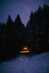 Poster - Beautiful view of snow groomer coming out of wood trees with a blue sky at evening