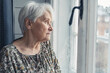 grey-haired caucasian pensioner lady looking sadly out of the window medium close up indoor shot. High quality photo