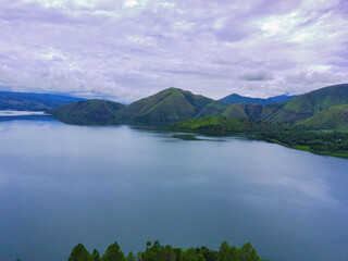 Wall Mural - Drone shot of a blue lake and green wooded mountains on a cloudy day