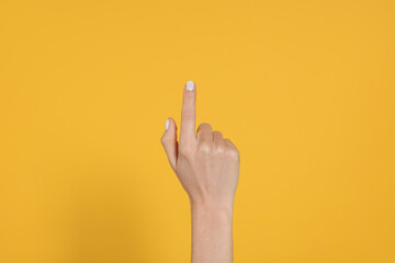 Wall Mural - Woman pointing at something against yellow background, closeup on hand