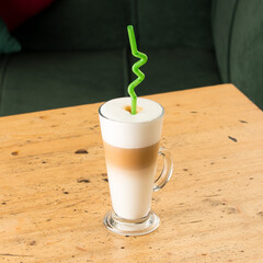 Poster - Gourmet foam latte with a green straw on a wooden table