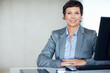 © STEEX/peopleimages.com - Confident business woman at office. Portrait of confident female executive smiling at office desk.
