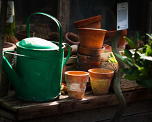 Old Green Watering Can And Empty Plant Pots Under The Sunlight In The Garden