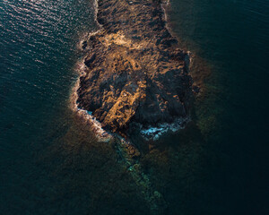 Bird's eye view of a rock peninsula being washed by ocean waves