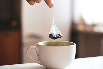 person's hand holding a tea bag and making hot cup of tea