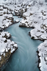 Poster - Vertical shot of a narrow, bendy river flowing through snow-covered rocks in winter