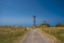 Empty Road Leading To An Island In Croatia Surrounded By Electrical Pylons On A Sunny Day