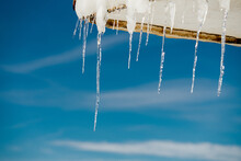 Closeup Of Icicles And Snow On A Roof Of A Building Under A Blue Sky And Sunlight
