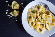 Top View Of Tortellini Pasta With Fork In A White Plate And Two Pieces Of It On Dark Blue Table