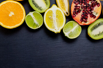 Wall Mural - Top view of halves of orange, kiwi, lemon, lime, banana and pomegranate on a black wooden table