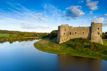 Canvas Print - Aerial shot of Carew Castle with a reflection on a river and a green valley under a cloudy blue sky