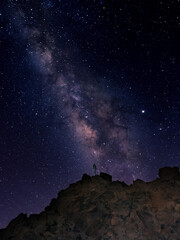 Wall Mural - The sky in the dark with a lot of shiny stars in it and a man standing on the mountain