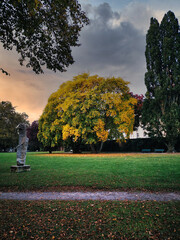 Sticker - a beautiful green garden with a big yellow tree in the middle and statues on the side