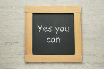 Wall Mural - Small chalkboard with motivational quote Yes you can on white wooden background, top view