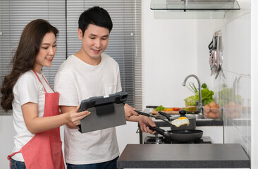 Wall Mural - couple cooking and preparing food according to a recipe on a tablet computer in the kitchen at home