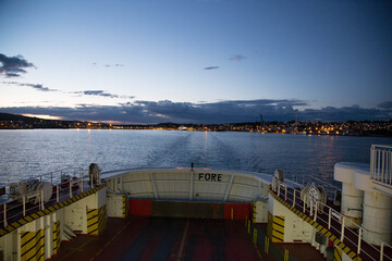 Wall Mural - Boat in a river or lake surrounded by town lights in the evening