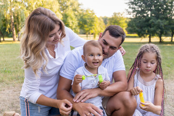 full family with son and daughter relax in park at sunset with rays of sun in summer and they launch soap bubbles. Dad, Mom, Kids full family Weekend leisure. School holidays. Family values. Love