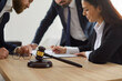 © Studio Romantic - Close up of judge's gavel against background of lawyer and client signing legal contract. Meeting of team in office of law firm that provides legal advice to clients. Selective focus.