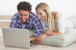 © Nicola K/peopleimages.com - Need a new couch Its just a click away. A happy young couple lying on the floor at home and using a laptop together.