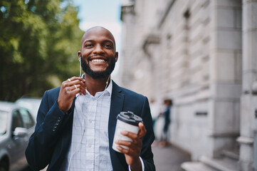 Wall Mural - This coffee break has me feeling inspired again. Shot of a businessman holding a coffee and listening to music through earphones while walking through the city.