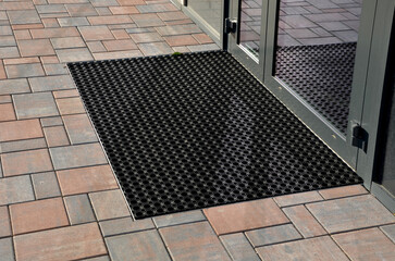 industrial mat cleaning zones at the entrance to the building. A black plastic-metal mat in the shape of an arch or half-circle lies on the limestone mosaic tiles