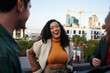 © StratfordProductions - Biracial female laughing, having a good time with group of multi-cultural friends socializing on a rooftop terrace at dusk.