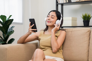 Relaxing time in living room. Beautiful young asian woman choose music from smartphone take a rest and listening song with headphone. Lifestyle in living room at house in the morning.