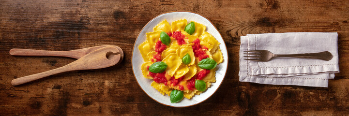 Wall Mural - Ravioli with tomato sauce and basil on a plate, overhead flat lay panorama. Italian dinner on a rustic wooden background panoramic banner