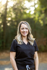 A medical professional with black scrubs with long hair outside in a natural background with copy space