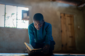 African teenage boy sitting and reading book in poor school, high quality photo