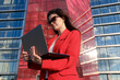 © makedonski2015 - Young woman typing on a laptop in front of an office building