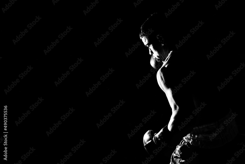 Young man practicing shadow boxing over black background. Black and white high contrast image. Strenght and motivation.