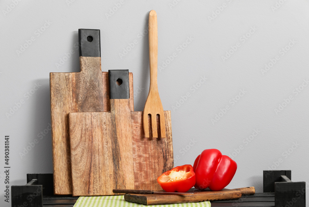 Wooden cutting boards, spatula and bell pepper on table near light wall