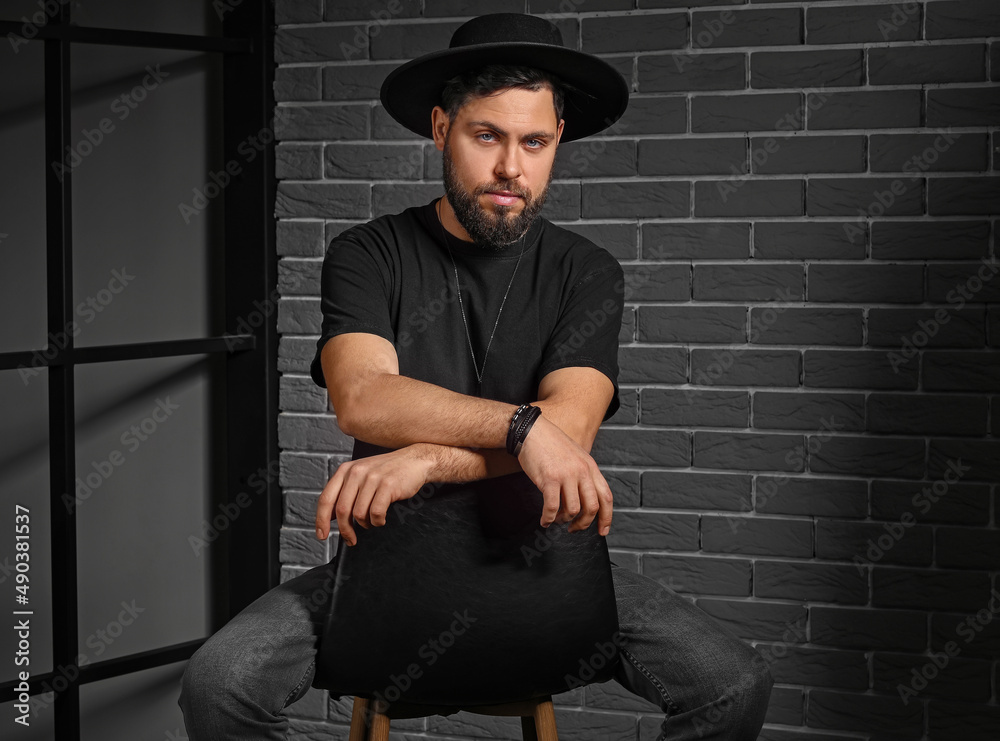 Stylish bearded man sitting on chair against dark background