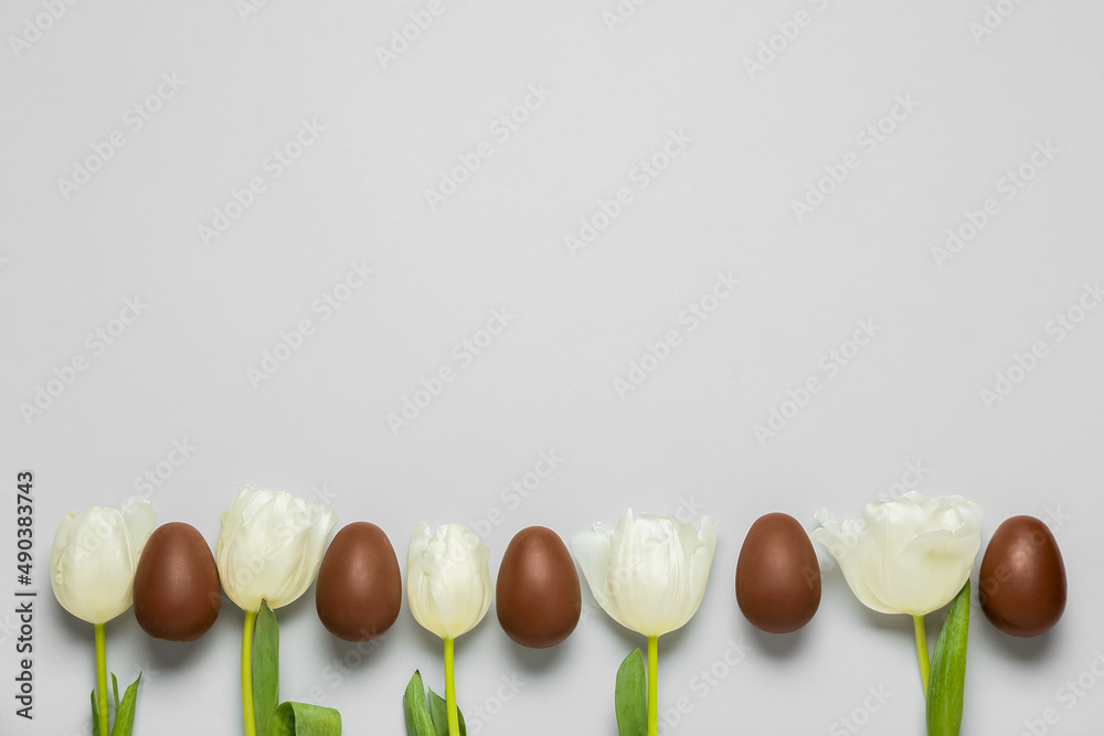 Delicious chocolate eggs and beautiful tulip flowers on light background
