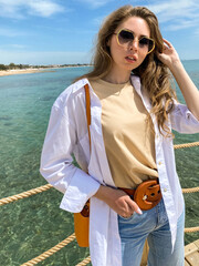 Wall Mural - Young blonde woman in casual clothes, jeans on the background of a beautiful blue sea. Vacation spring concept