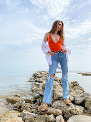 Wall Mural - Young blonde woman in casual clothes, jeans on the background of a beautiful blue sea. Vacation spring concept