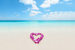 Heart shape lei flowers on perfect white sand beach for Hawaii honeymoon romantic vacation getaway travel. Pink orchids flower necklace lying on paradise background.