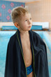 © ninelutsk - Child wrapped in towel near indoor kid swimming pool waiting for lesson. Toddler boy after training wet near water in swimwear on edge of swimming pool