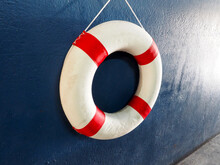 White With Red Stripes Lifebuoy Or Saver Ring Hanging On Navy Blue Wall