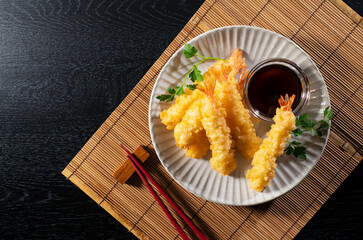 Shrimp tempura on a plate placed against a black background.