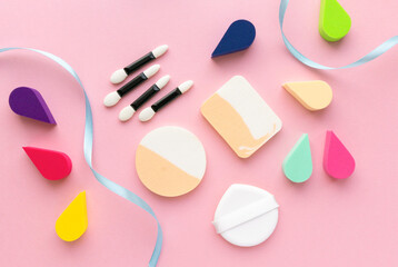 Makeup flat lay. Various foundation sponges and eyeshadow applicators on pink background